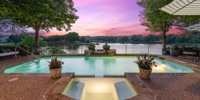 Backyard view overlooking the pool and lake with a beautiful sunset painting the sky colors of pink, purple, and blue.